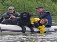 Picture of black Newfoundland dog with paws on edge of boat as smiling owner encourages it to leave