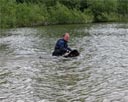 picture of black newfoundland dog swimming alongside owner who is now waist deep in water