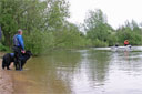 picture of owner and Newfoundland dog stood waiting on shore whilst boat with retrieve object approaches